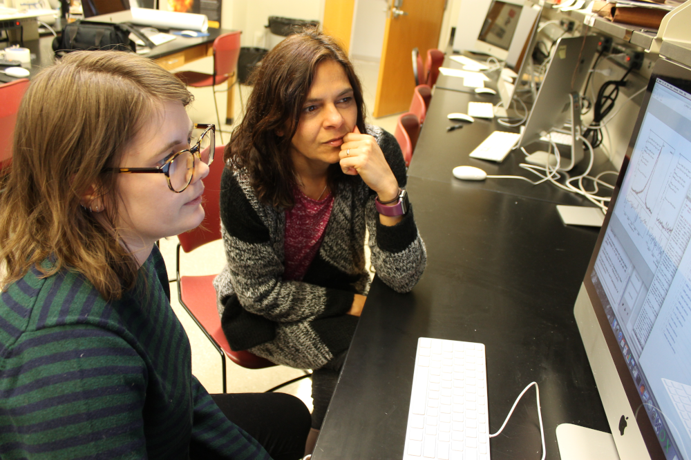 Anca Constantin and Jenna Harvey seated side by side and looking at a computer screen with line graphs and charts.